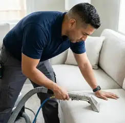 Professional upholstery cleaning technician using an extraction wand to deep-clean a fabric sofa, Manchester, NH.